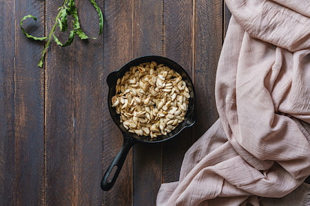 A cast iron pan with pumpkin seeds on a dark wood table